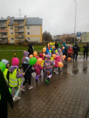chodnikiem idą dzieci i trzymają kolorowe balony na przodzie dwóch policjantów