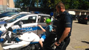 na policyjnym parkingu dziecko na motocyklu, policjant obok, radiowozy