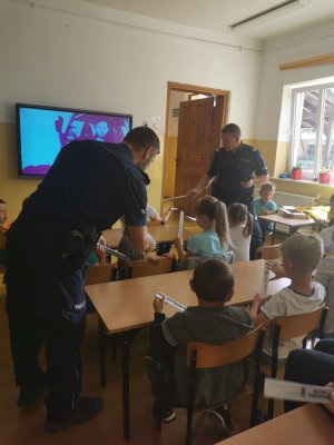 policjanci w klasie rozdają dzieciom opaski odblaskowe