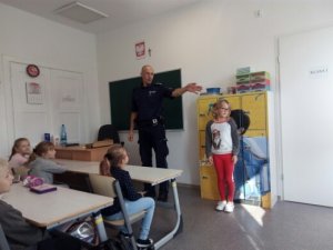 policjant w klasie wraz z dzieckiem pokazuje jak rozglądać się