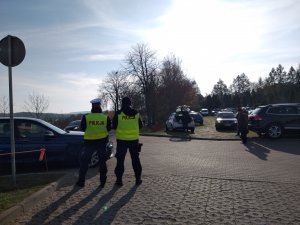 Parking przy cmentarzu na Polskiej Wsi. W tle  policjanci w kamizelkach odblaskowych.