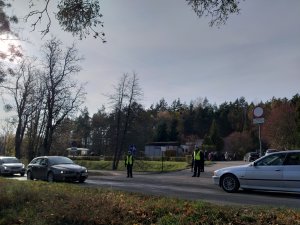Pierwszy parking przy cmentarzu na Polskiej Wsi i ulica. W tle  policjanci w kamizelkach odblaskowych.