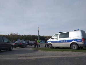 Parking przy cmentarzu na Polskiej Wsi. W tle stoi policyjny radiowóz i policjanci w kamizelkach odblaskowych.