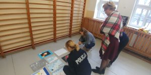 policjanci pracownicy oglądają prace plastyczne w szkole rozłożone na podłodze