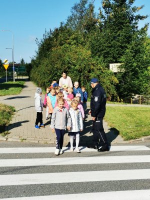 policjant stoi z dziećmi przy przejściu dla pieszych