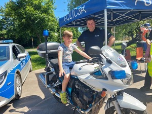 chłopiec siedzący na motocyklu policyjnym i stojący przy nim policjant