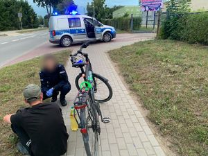 mężczyzna przy rowerze siedzący na chodniku, przy nim klęczy policjant w tle radiowóz policyjny