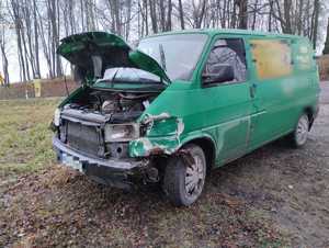 samochód VW Transporter koloru zielonego z podniesioną maską i uszkodzonym przodem stojący na nieutrawdzonym gruncie