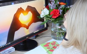 siedząca przed komputerem kobieta, na ekranie komputera wyświetlają się ułożone dłonie w kształcie serca