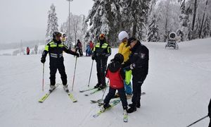 dorośli i dzieci w kombinezonach narciarskich i nartach stoją na ośnieżonym terenie