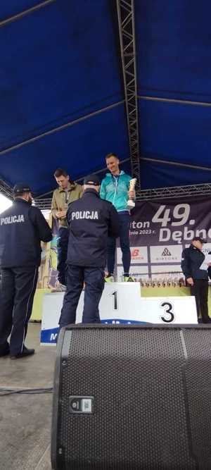 mł.asp. Rafał Syczew na najwyższym stopniu podium z pucharem i medalem, stojący przed nim dwaj policjanci