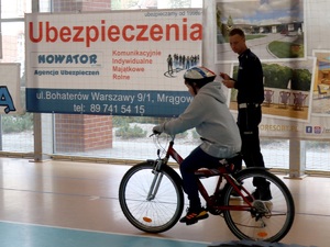 na hali sportowej chłopiec jadący w kasku rowerem, obok idzie policjant