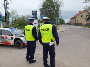 dwóch policjantów ruchu drogowego stojący na chodniku przy skrzyżowaniu obok przejeżdża rajdówka