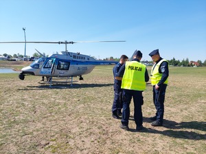 trzech rozmawiających policjantów, w tle helikopter policyjny