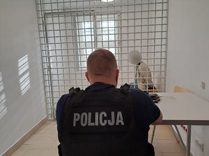 siedzący za kratami mężczyzna i siedzący przy biurku policjant