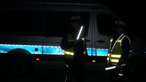 noc, policjanci w kamizelkach odblaskowych trzymają odblaski
