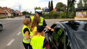 przy ulicy w Marcinkowie policjant w kamizelce odblaskowej podaje alkoblow kierowcy obok stoją dzieci w kamizelkach odblaskowych