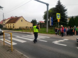 na ulicy policjant kieruje ruchem, dzieci stoją przed pasami