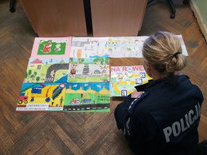 na podłodze leżą prace plastyczne laureatów konkursy - 9 . ogląda je policjantka