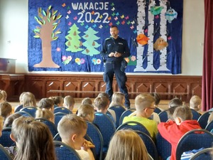 policjant stoi na podeście na krzesełkach siedzące dzieci