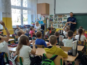 policjant w SP nr 4 w Mrągowie opowiada dzieciom siedzącym na krzesełkach o zasadach bezpiecznego spędzania wakacji