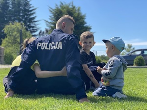 policjant siedzący tyłem na trawie z trójką swoich dzieci