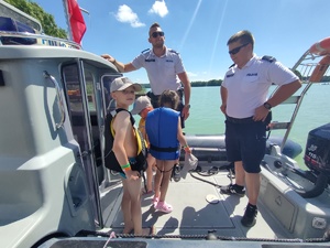 dwóch policjantów i dwoje dzieci stojących na łodzi policyjnej