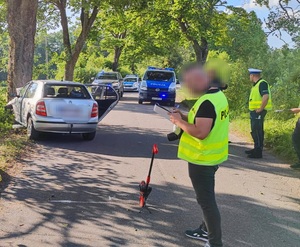 policjant sporządzający dokumentację, w tle rozbite auto i radiowozy policyjne