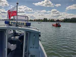 łódź policyjna w tle inne łódki i osoby płynące w jeziorze