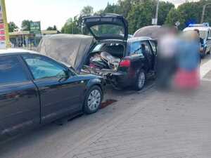 dwa ciemne samochody stojące jeden za drugim, samochód stojący z tyłu ma podniesioną maskę a samochód stojący z przodu ma podniesioną klapę bagażnika