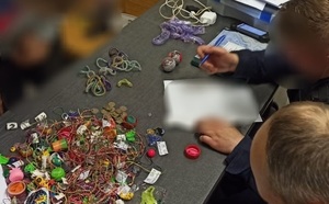 policjant siedzący przy biurku, na biurku leżące gadżety- zabawki, koraliki