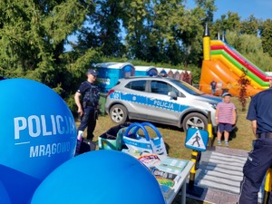 policjanci stojący przy miasteczku umiejętności drogowych na pierwszym planie balony z napisem Policja Mrągowo, w tle radiowóz policyjny