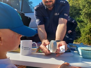 policjant z lupą pokazuje dziecku odbitkę jego palca