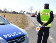 przód radiowozu policyjnego i policjant w żółtej kamizelce stojący tyłem