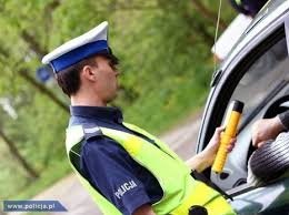 policjant trzymający w ręce alkomat stojący przy samochodzie