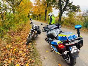 stojący na drodze motocykl policyjny, obok policjant, przed nim stoi motocykl