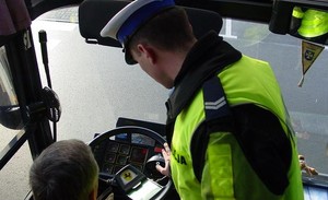 na zdjęciu widać policjanta ruchu drogowego pochylającego się nad kierownicą autobusu, przy kierownicy siedzi kierowca autobusu