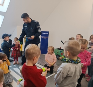 na sali odpraw komendant podaje dłoń dziecku, inne dzieci stoją wokół, mają w rękach opaski odblaskowe