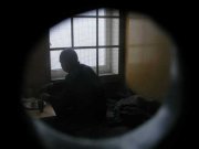 widok przez wizjer w drzwiach na osobą siedzącą przy oknie z kratami