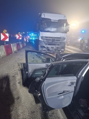 z prawej strony stoi samochód z otwartymi drzwiami przed nim stoi samochód ciężarowy z rozbitym orzodem