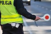 policjant w żółtej kamizelce z "lizakiem policyjnym" w ręce stojący przy drodze