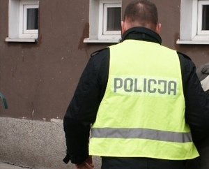 policjant w żółtej kamizelce z napisem na plecach policja przed budynkiem