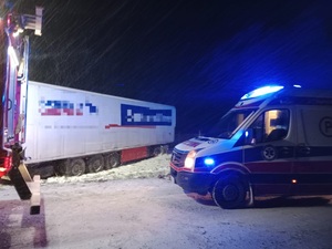na drodze z prawej strony stoi karetka pogotowia z włączonymi sygnałami świetlnymi, przed nią stoi wóz strażacki, z prawej strony w polu naczepa samochodu ciężarowego