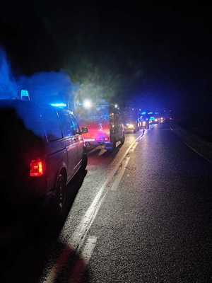 samochody służb ratunkowych z włączonymi sygnałami świetlnymi nocą stojące na pasie ruchu