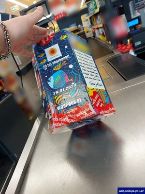 na ladzie sklepowej dłoń przechylająca puszkę wośp, w tle wnętrze sklepu