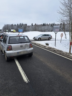 na drodze stojący pojazd seat z wgnieceniem tylnej klapy, z prawej strony w bocznej drodze stoi srebrny pojazd osobowy