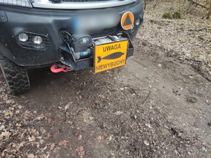 w lesie stojący wóz saperski z żółtą tabliczką z przodu z napisem uwaga niewybuch