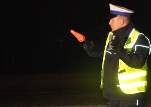policjant ruchu drogowego w żółtej kamizelce trzymający w ręku latarkę ze świecącą czerwoną nakładką