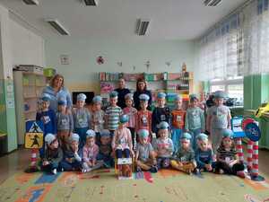 siedzące w sali dzieci a za nimi stojące dwie policjantki. Po bokach stoją wychowawczynie grupy. Na środku na krzesełku siedzi dziewczynka a przed nią stoi misiaczek rozrabiaczek zamknięty w więzieniu.