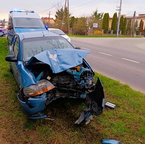 stojący na poboczu drogi samochód koloru niebieskiego z rozbitym przodem a za nim stojący radiowóz policyjny